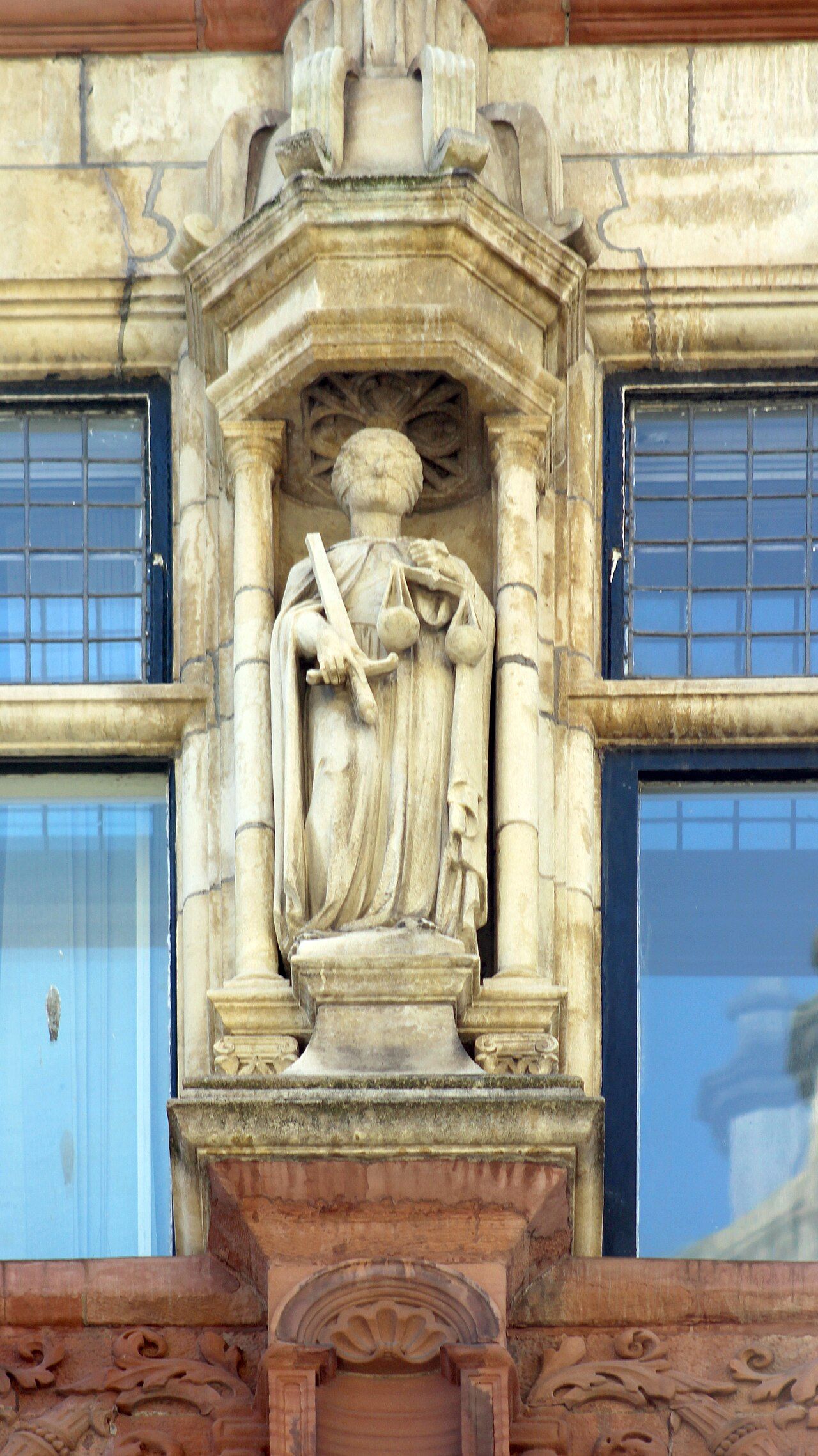 A statue of Justice holding balanced scales, blindfolded, against a stone courthouse façade.