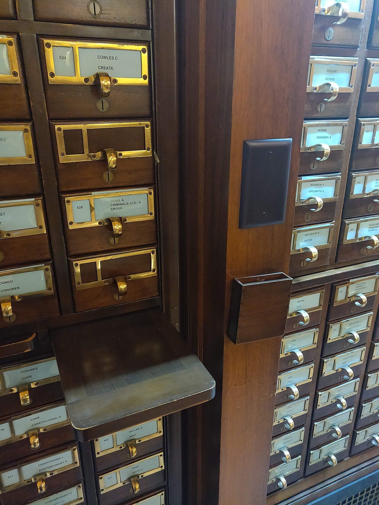 A wooden library card catalog with a drawer pulled open, revealing tightly packed index cards with typed bibliographic entries