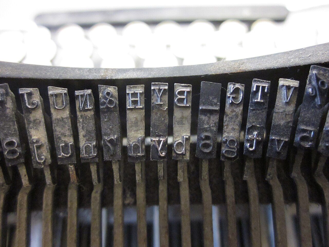 Close-up of metal typewriter typebars showing letter and numeral slugs in mirror image