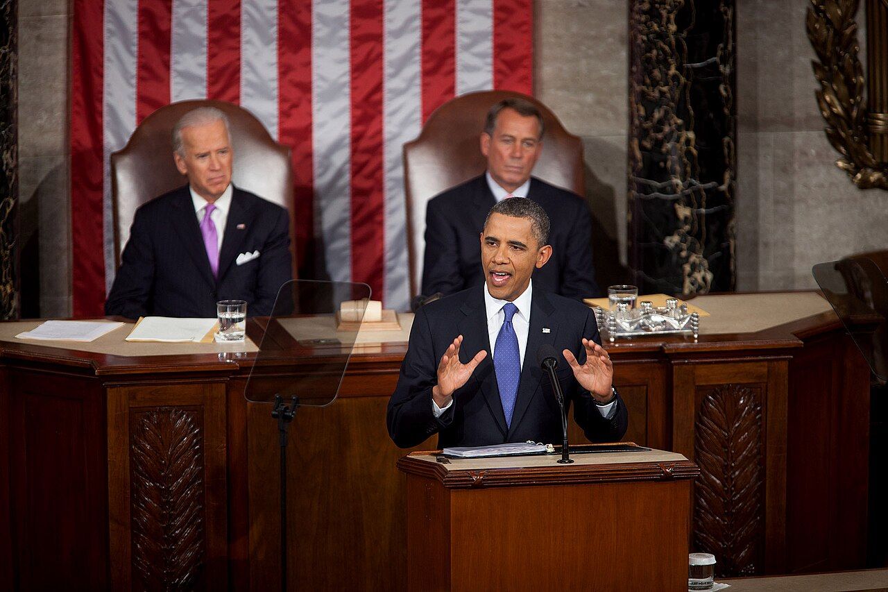A speaker at a lectern addressing a seated audience in a lecture hall